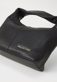 Svart läderhandväska med texturerad yta, halvcirkelformad öppning för handtag och guld "Valentino"-logotyp på framsidan. Rektangulär form.