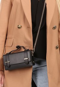 Zwarte leren handtas met een gestructureerde rechthoekige vorm, gouden hardware-accenten, een detachabele kettingriem en een bovenhandvat.