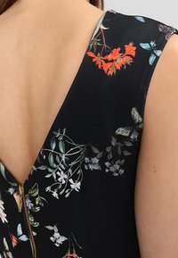Robe noire à motifs floraux avec un décolleté en V profond et une fermeture éclair. Le tissu présente des motifs de fleurs colorées et de papillons sur un fond sombre.