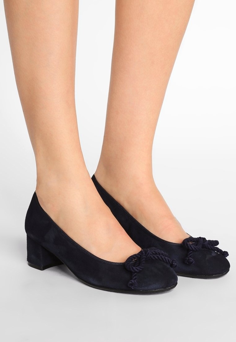 Marinblå mocka låga klackskor med rund tå och dekorativa knutdetaljer framtill. Slät textur och enkel design.
