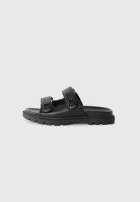 Black slide sandal made of smooth leather, featuring two adjustable straps with circular hardware. The sole is textured for grip.