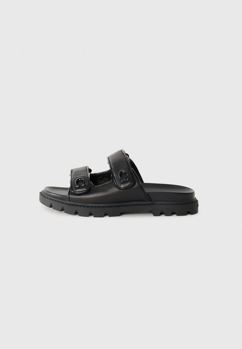 Black slide sandal made of smooth leather, featuring two adjustable straps with circular hardware. The sole is textured for grip.