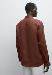 Rust-colored linen shirt with a relaxed fit, long sleeves, and a classic collar. Features buttoned cuffs and a smooth texture.