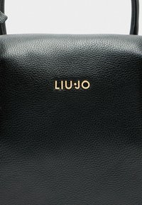 Zwarte leren handtas met een gestructureerd oppervlak, gouden logo "LIUJO," en een minimalistisch design. Compacte vorm met een bovenhandvat.