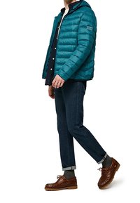 Blågrön puffjacka med horisontell quiltning, framförsdragkedja och huva. Bärs över en blå skjorta, ihop med mörka jeans och bruna båtshoes.