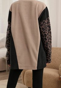 Sudadera de manga larga y corte oversize, con un panel central suave en color beige, laterales negros y mangas con estampado de leopardo. Tejido suave y texturizado.