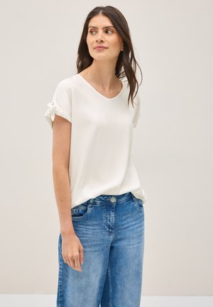 Witte, kortebloezermouw V-hals top met decoratieve strikjes op de mouwen, gecombineerd met lichtblauwe wijde jeans. Glad textuur, casual ontwerp.