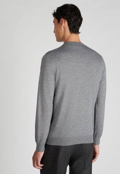 Grauer Strickpullover mit langen Ärmeln, rundem Halsausschnitt und ribbeligen Bündchen. Glatte Textur und schlichtes Design. Getragen mit dunklen Hosen.