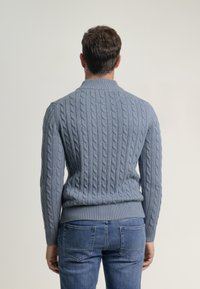 Suéter de punto trenzado en azul claro, con cuello y dobladillo acanalados. Ajuste cómodo con un patrón texturizado en la espalda, combinado con jeans de mezclilla.
