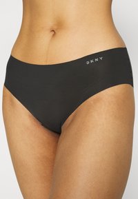 Črne hipsterske hlačke DKNY so narejene iz gladkega materiala, imajo brezšivno zasnovo in diskreten logotip na pasu, brez vidnih šivov.