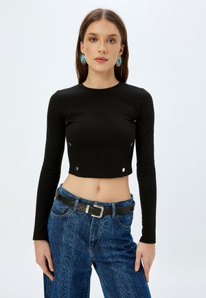 Zwarte lange mouwen cropped top met drukknopen. Gecombineerd met blauwe jeans en een zwarte riem met een studded ontwerp.
