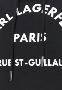 Černá mikina s kapucí s bílým textem "Karl Lagerfeld Paris" a kulatým vzorem loga. Obsahuje splétané šňůrky s kovovými konci.