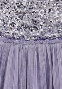 Levendulaszínű ruha, amely flitteres felsőrésszel rendelkezik, ezüst és lila flitterekkel, redőzött derékrésszel és légies tüllszoknyával a térfogat és a textúra érdekében.