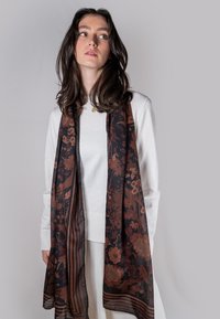 Bufanda negra transparente con un patrón floral en tonos marrones y acentos a rayas, drapeada alrededor de una persona que lleva una blusa blanca.