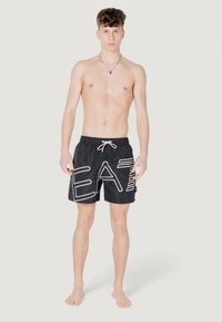 Bañador negro con letras en blanco que dicen "COMER", cinturilla con cordón y una textura suave, combinado con un diseño ajustado hasta el muslo.