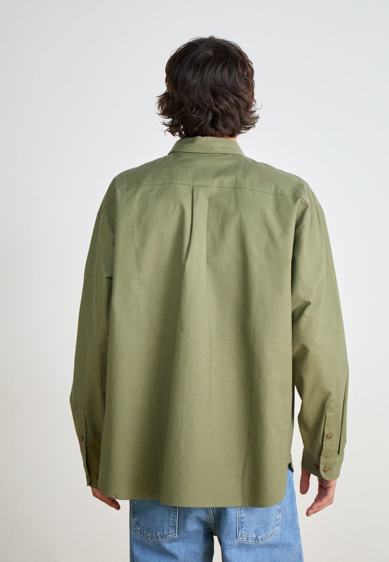 Camisa de manga larga verde oliva hecha de algodón, con cuello y puños abotonados, de corte relajado y detalle de pliegue en la parte posterior.