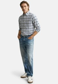 Blau-weiß kariertes Hemd, Jeans und weiße Turnschuhe mit schwarzen Akzenten. Das Hemd hat einen Kragen und hochgekrempelte Ärmel.