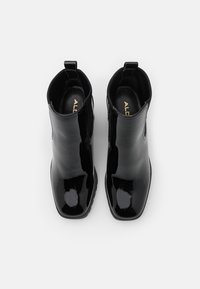 Botas de tobillo de charol negro con un diseño elegante, paneles laterales elásticos y tiradores en la parte posterior para facilitar su puesta. Forma de punta cuadrada.