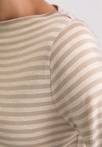 Beżowy sweter w paski z delikatnymi poziomymi liniami; posiada okrągły dekolt i gładką teksturę na szwie ramion.