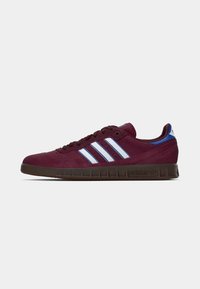 Burgundy mockask sneaker med tre vita ränder, blå accenter och en strukturerad brun gummisula. Lågprofil design med rundad tå.