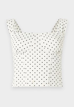 Débardeur blanc court à larges bretelles avec motif à pois noirs, présentant un décolleté en cœur et des coutures structurées au niveau de la poitrine.