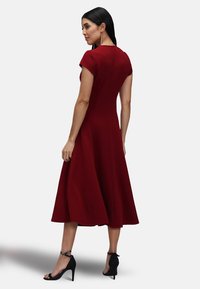 Red A-line dress with short sleeves, fitted bodice, and flared skirt. Smooth fabric, knee-length, paired with black heels.