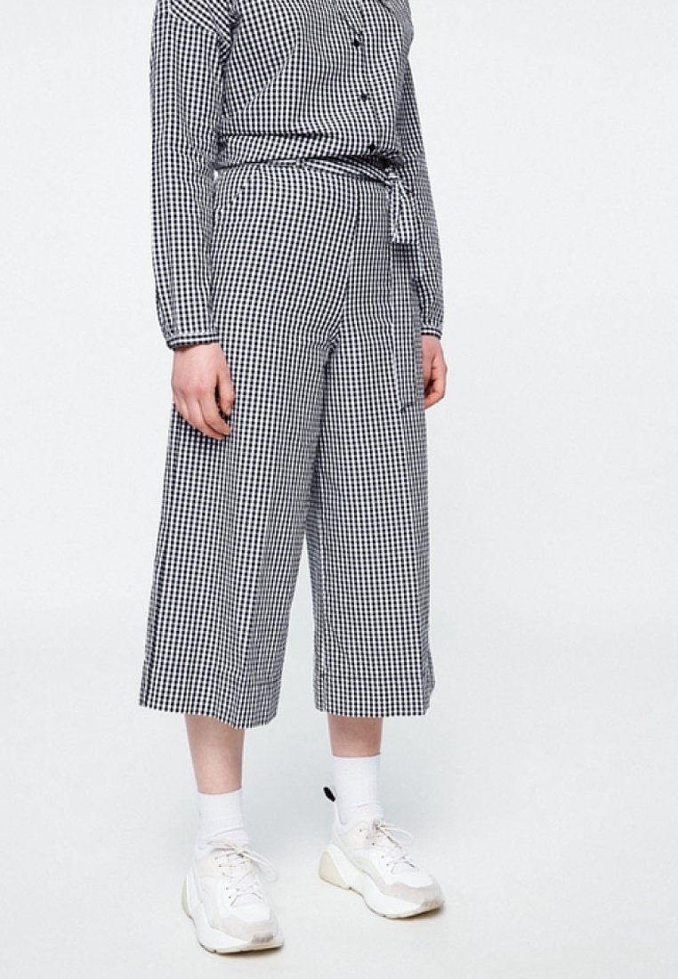 Musta-valkoinen ruudullinen gingham-paita ja lyhyet housut. Nappikiinnitteinen kauluksellinen paita, jonka vyötäröllä on vyö, löysä istuvuus ja sivutaskut. Yhdistetty valkoisiin tennareihin.