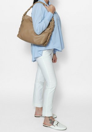 Bruine leren schoudertas met gevlochten handvat, zachte textuur, van gemiddelde grootte, gecombineerd met een casual blauw shirt en witte broek.