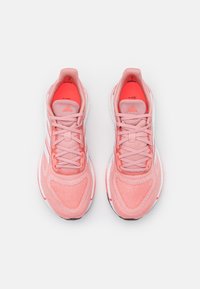 Chaussures de sport roses avec une tige texturée, des bandes blanches contrastantes et un bout arrondi. Accents réfléchissants au talon et sur la languette.