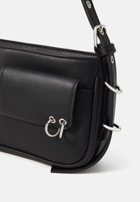 Borsa a spalla in pelle nera con tasca frontale, hardware argentato, bordi arrotondati e tracolla regulabile, caratterizzata da accenti a forma di anello circolare.