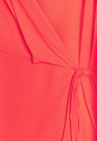Tessuto corallo brillante con una consistenza morbida, caratterizzato da elementi di design drappeggiati e un accento annodato sul lato.