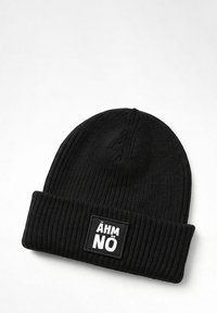 Black knit beanie with ribbed texture. Features a stitched rectangular patch with "ÄHM NO" in white lettering. Rounded top design.