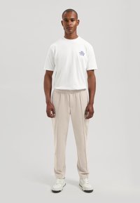 Hvit bomulls-T-skjorte med teksten "NO. STREET CLUB", kombinert med lysebeige sweatpants med elastisk midje og hvite joggesko med svarte såler.