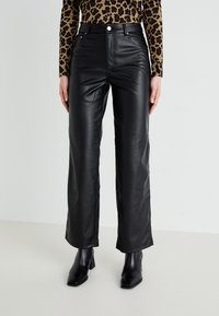 Pantalons en simili cuir noir avec une taille haute, une coupe évasée, des poches avant et des éléments en métal argenté visibles. Texture lisse et finition soignée.