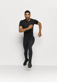 Camisa atlética negra y mallas, diseño ajustado con patrones texturizados, pose de carrera, zapatos negros resistentes, fondo neutro.