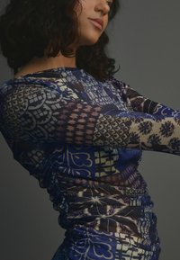 Robe ajustée �à manches longues avec un motif patchwork varié dans des tons de bleu, violet et crème. Tissu transparent avec des fronces texturées sur les côtés.