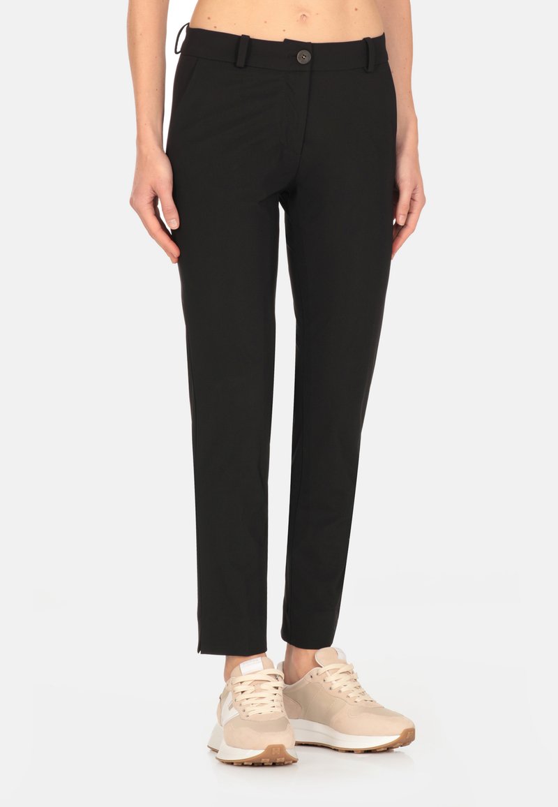 Pantaloni neri slim-fit realizzati in tessuto leggero. Presentano una chiusura con bottone, passanti per la cintura e tasche laterali. Abbinati a sneakers beige.