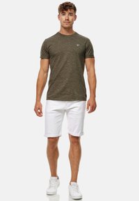 Olivgrünes strukturiertes T-Shirt mit kurzen Ärmeln, kombiniert mit weißen hochgekrempelten Jeansshorts und weißen Sneakers. Minimalistisches Design.