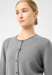 Šedý pletený cardigan s kulatým výstřihem, předními knoflíky a hladkou strukturou. Tkanina vypadá měkce a lehce.
