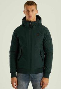 Temnozeleno zip-jakno s kapuco, ki ima dva sprednja žepka na zadrgo, rebrast rob in manšete ter majhen logotip na prsih.