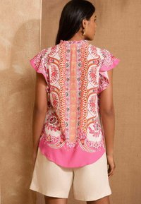 Blusa a maniche corte in tessuto leggero con motivi floreali rosa e arancioni, dotata di un pannello posteriore decorativo e maniche arricciate.