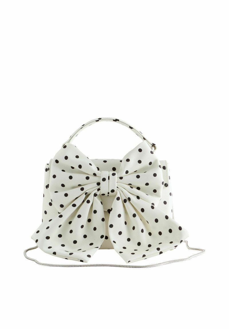 Sac à main blanc à pois noirs, grand nœud assorti à l'avant, poignée supérieure et fine bandoulière argentée.