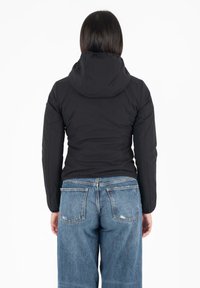 Giacca nera imbottita con cappuccio, caratterizzata da un design aderente, texture liscia e cuciture visibili, abbinata a jeans blu.