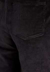 Črne kord hlače z navpičnim rebrastim vzorcem in zadnjim žepom pravokotne oblike. Tkanina je mehke teksture.