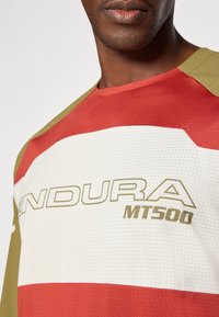 Maglia da ciclismo rosso, bianco e verde oliva caratterizzata da una texture a rete, con il logo "ENDURA MT500" in evidenza in lettere dorate.