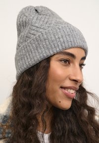 Bonnet en tricot gris avec une texture côtelée, présentant un sommet légèrement pointu et un Revers replié, affiché sur un fond neutre.