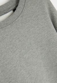 Szary sweatshirt z prążkowanym dekoltem i subtelną teksturowaną powierzchnią, z małym haftowanym logo z boku.