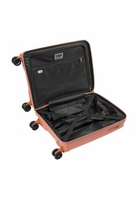 Valigia rigida di colore corallo, con interno nero, tasca con zip, cinghie regolabili e quattro ruote nere per la movimentazione.