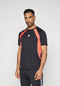 Tricou sport negru cu panouri laterale portocalii, guler rotund, mâneci scurte și un logo alb pe piept. Textură netedă.