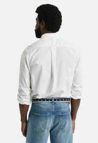 Weißes Hemd mit aufgerollten Ärmeln, von hinten betrachtet. Getragen mit hellblauen, ausgewaschenen Jeans und einem gemusterten dunklen Gürtel mit Segelbooten.
